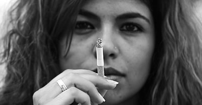Latina looking at camera while holding a lit cigarette