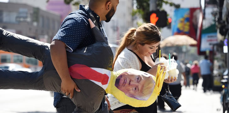 Two U.S. Latinos walking a President Trump effigy